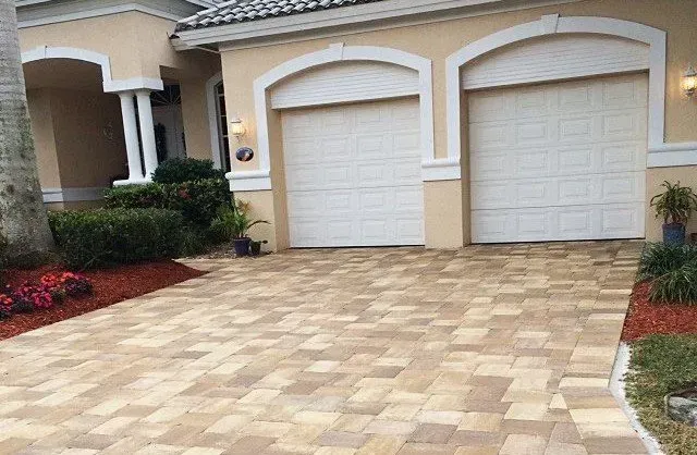A house with two garage doors and a brick driveway in front of it.