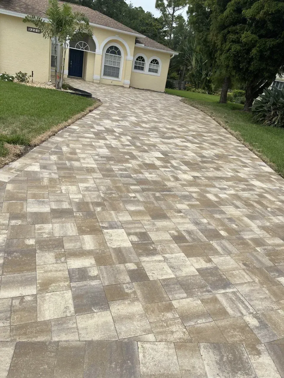 A brick driveway leading to a yellow house.