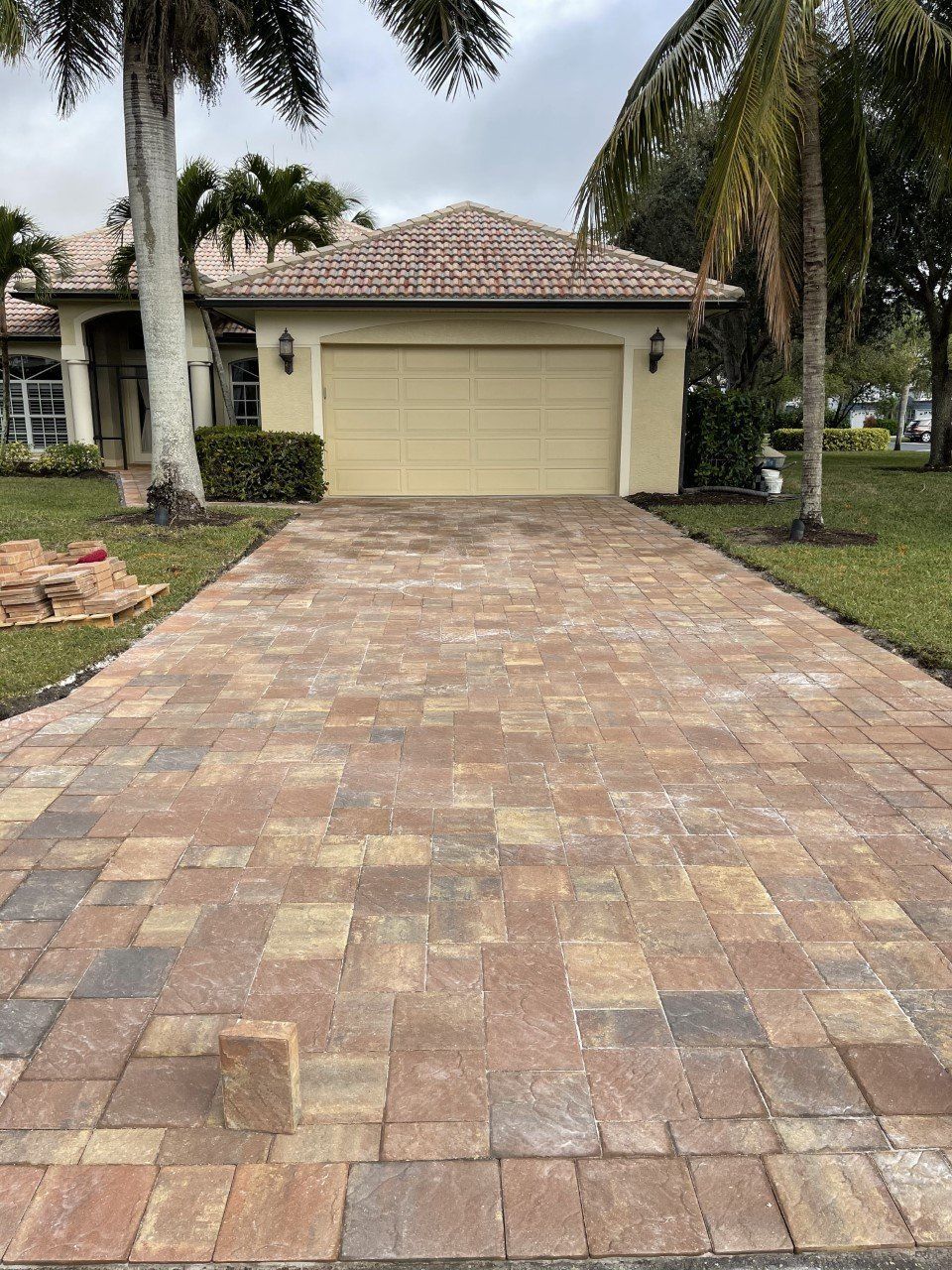 A driveway leading to a house with a garage and palm trees.