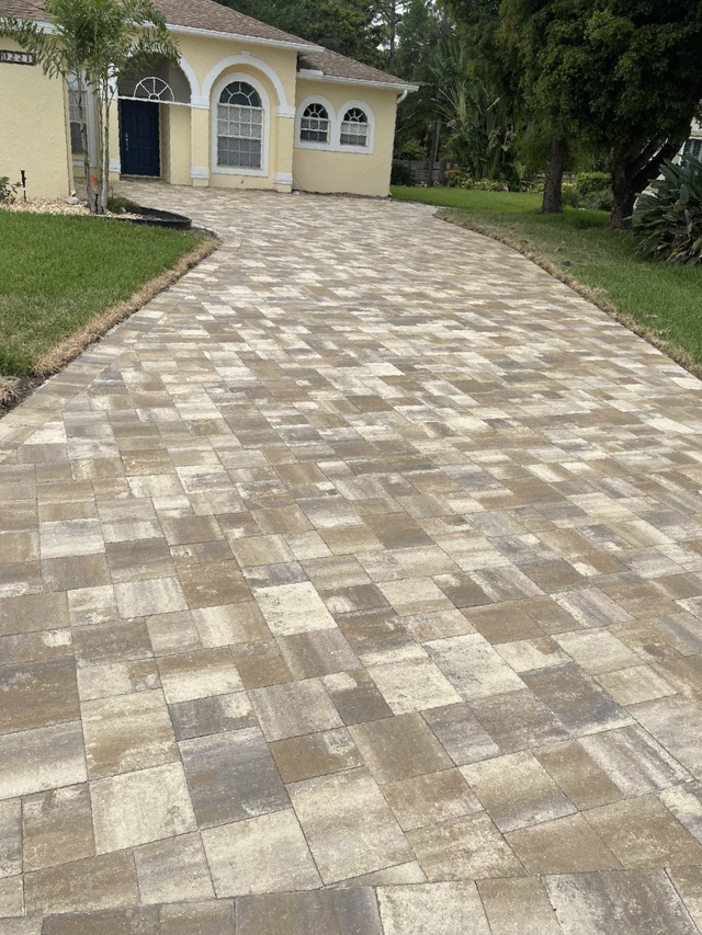 A brick driveway leading to a house with a lush green lawn.