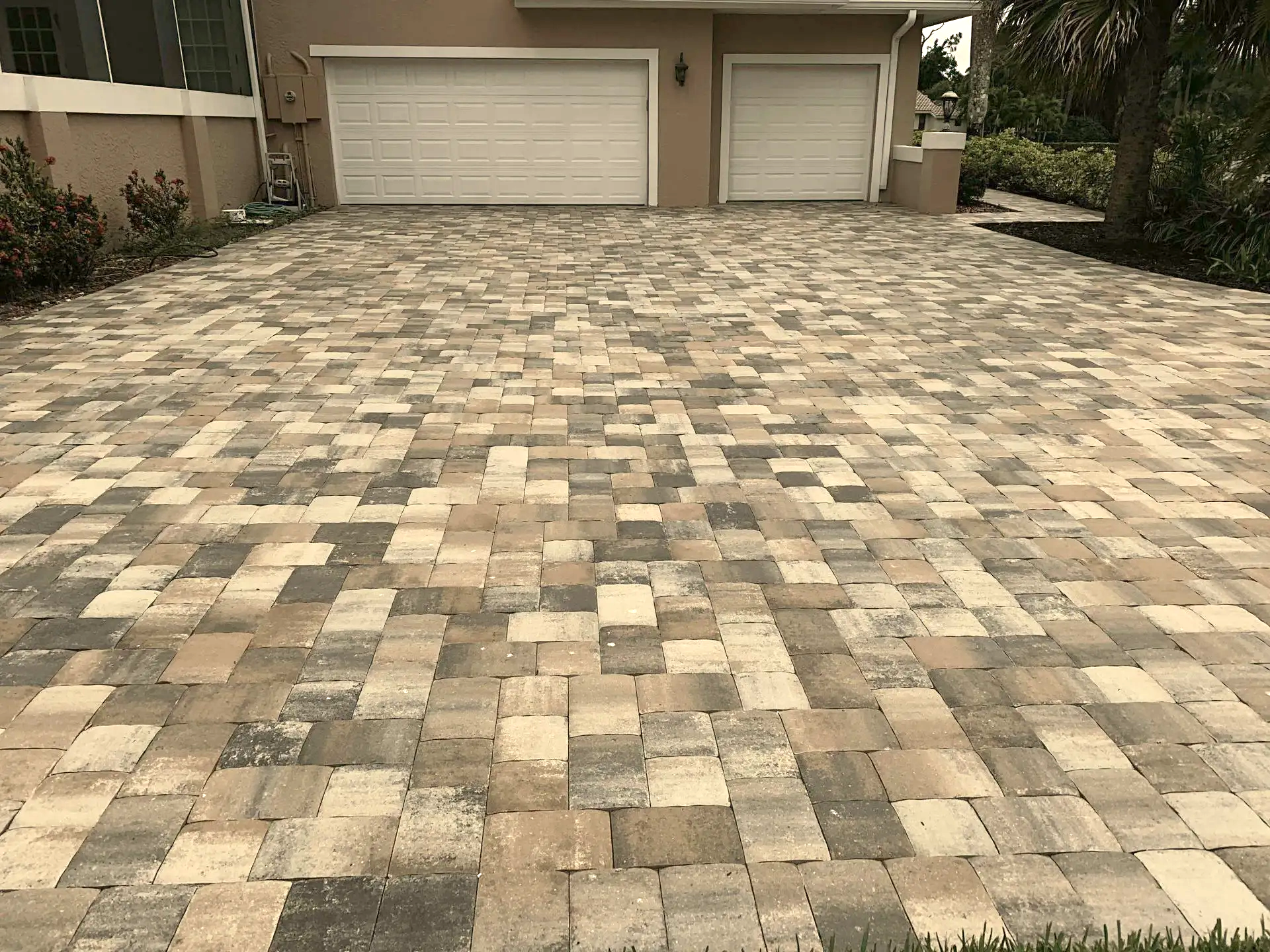 A brick driveway in front of a house with two garage doors.