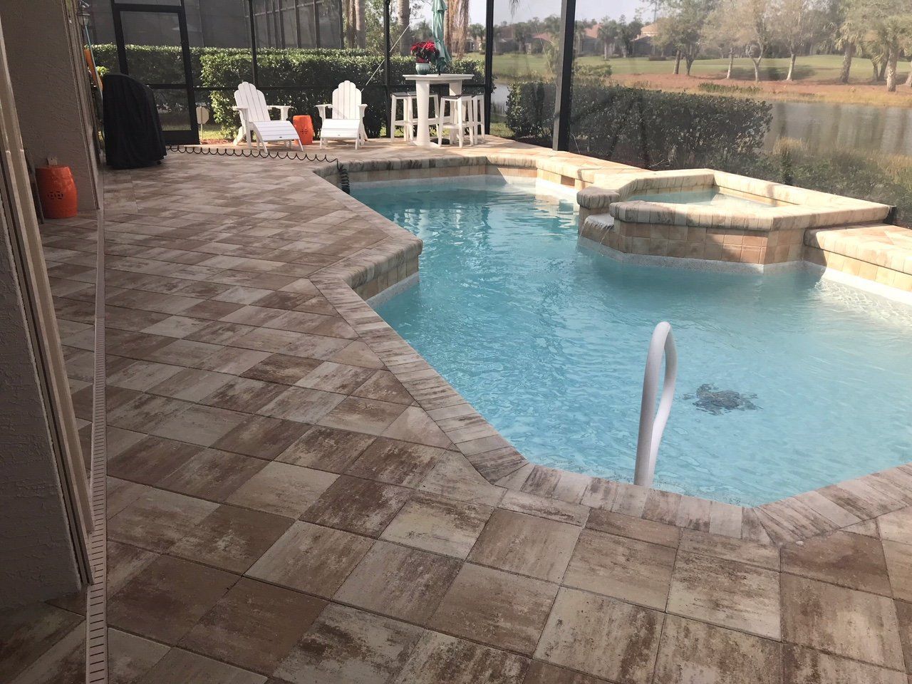 A large swimming pool is surrounded by a patio with chairs and a table.