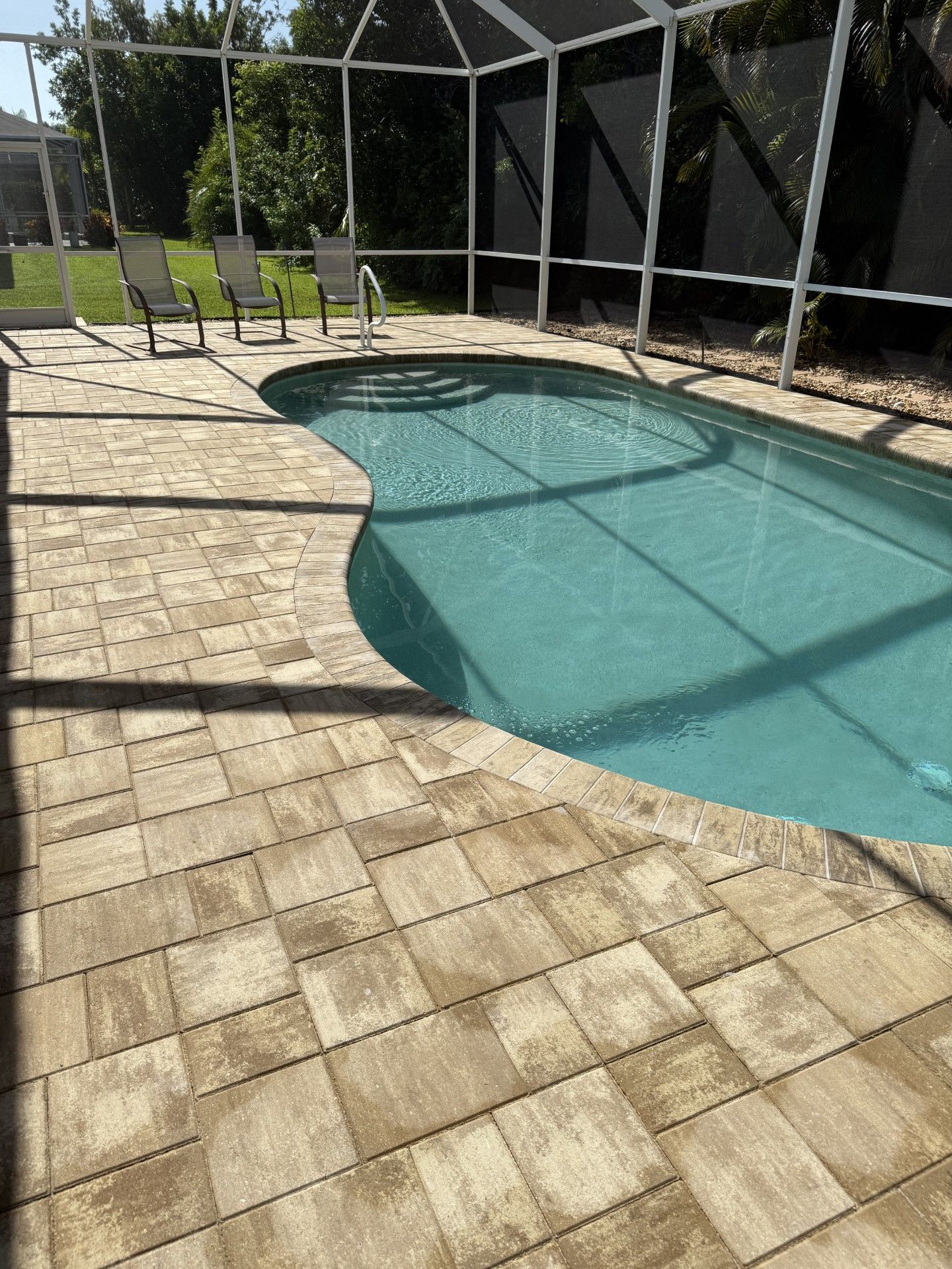 A large swimming pool surrounded by chairs and a screened in area.