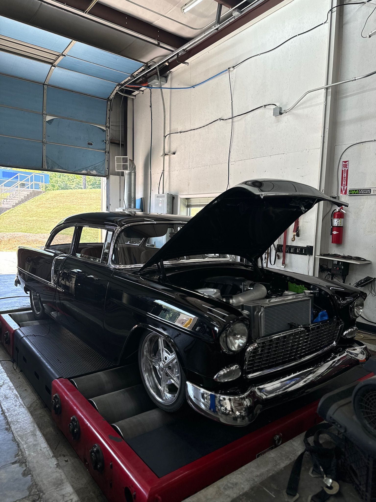 A black car with the hood up is parked in a garage.