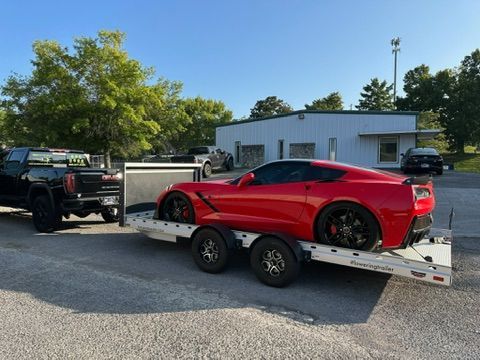 A red sports car is being towed by a truck on a trailer.