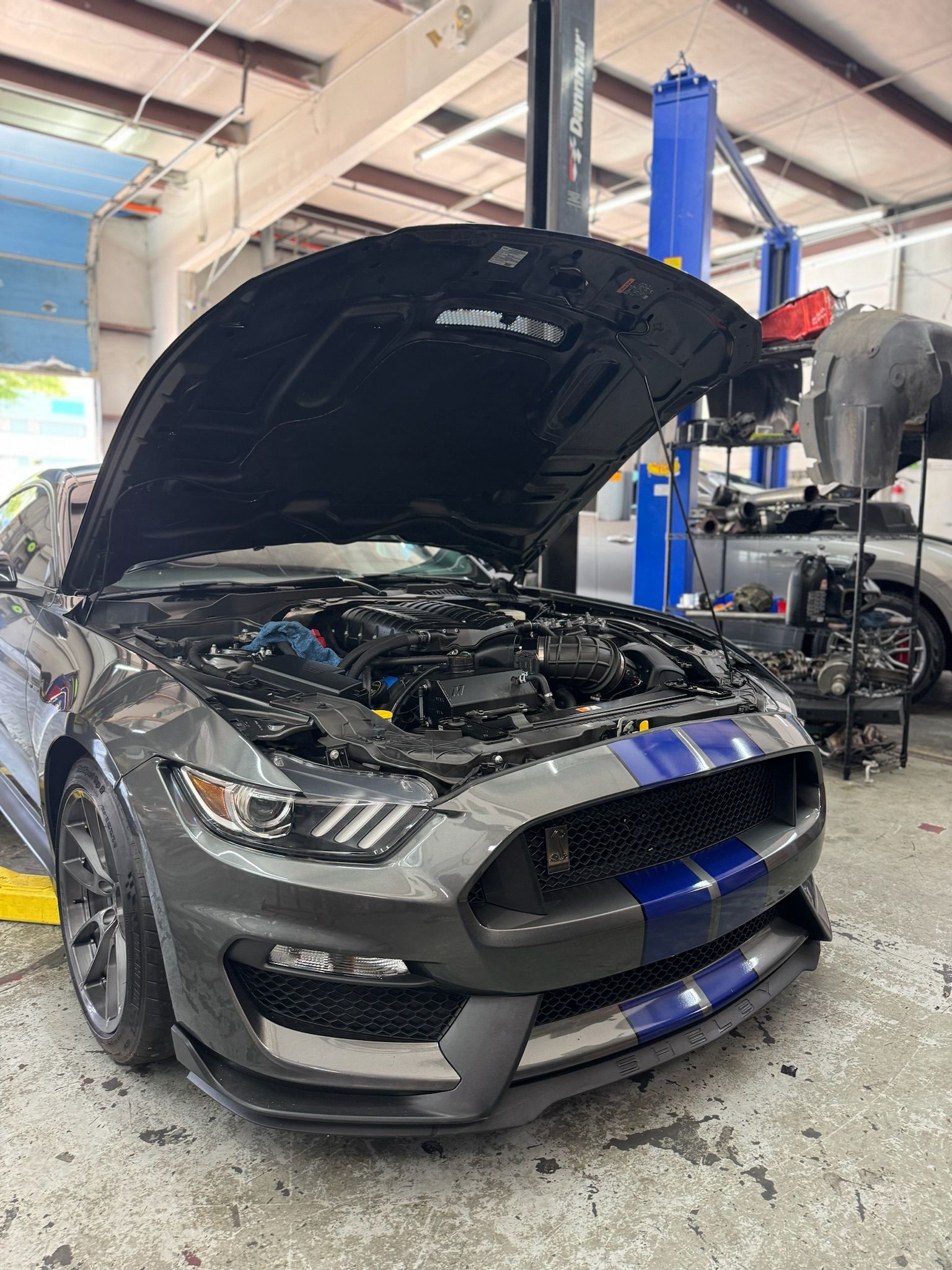 A gray ford mustang with its hood open in a garage.