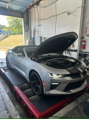A silver car with its hood up is sitting on a machine in a garage.