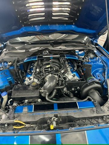 The engine of a blue mustang is shown with the hood open.