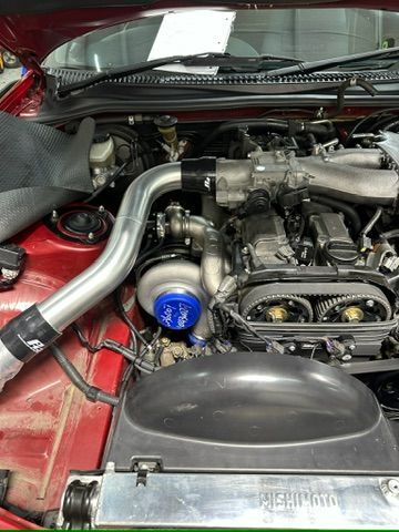 The engine of a red car with a turbocharger attached to it.