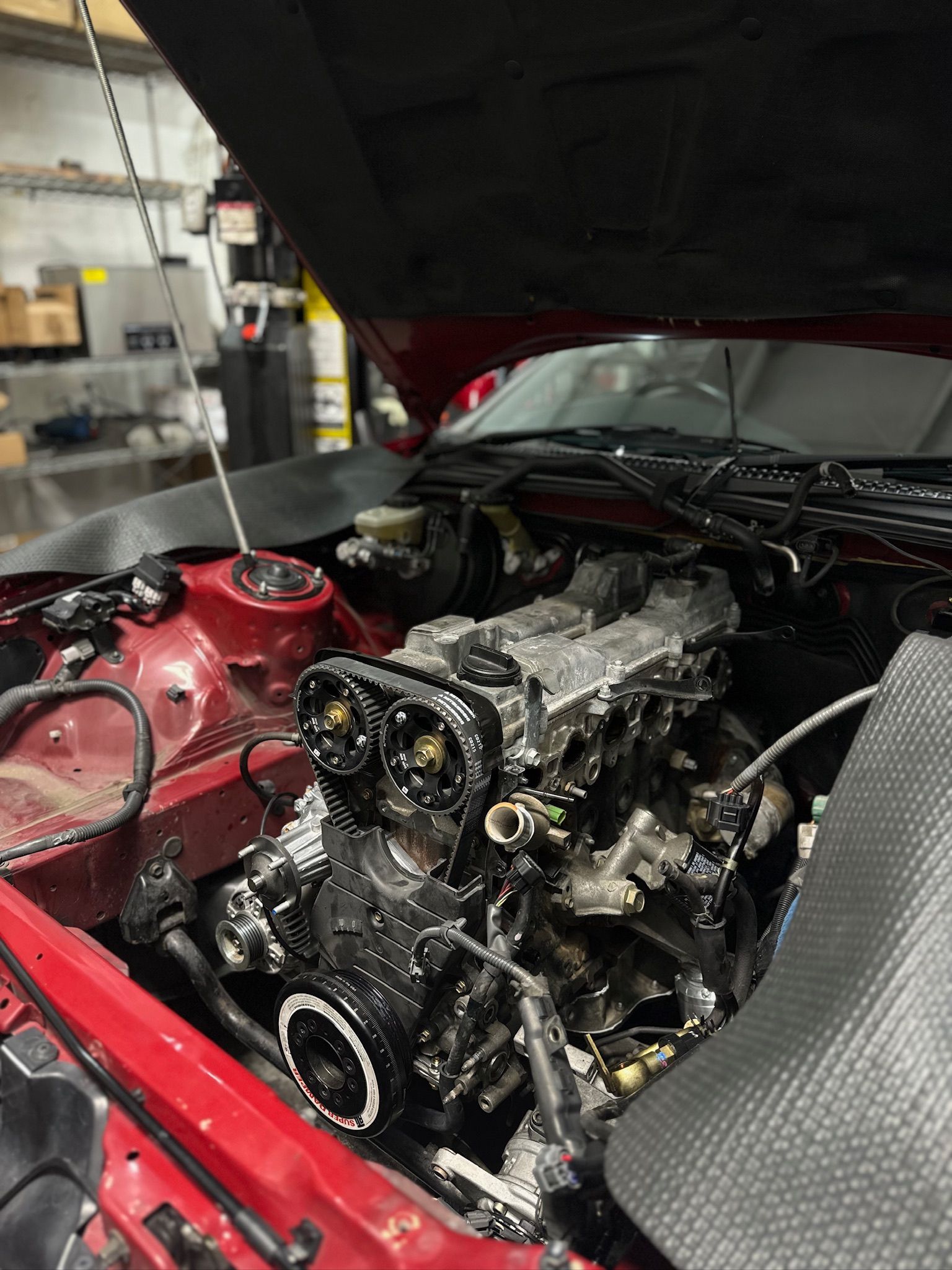 A red car with the hood open is being worked on in a garage.