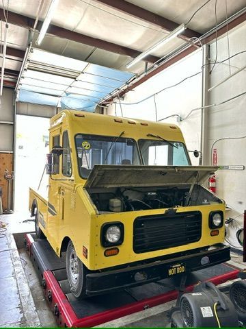 A yellow food truck is parked in a garage with its hood open.