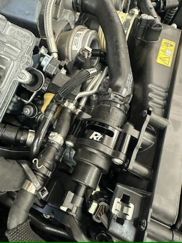 A close up of a car engine with a hose attached to it.