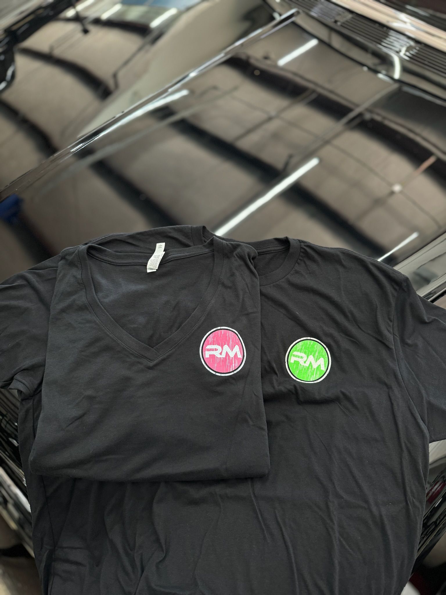 Two black t-shirts are sitting on top of a black car.