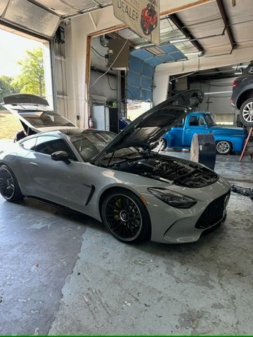 A gray sports car with the hood up is parked in a garage.