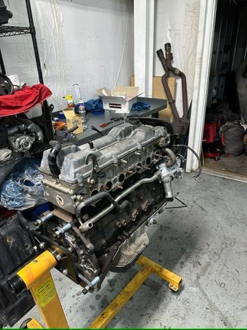 A car engine is sitting on top of a yellow stand in a garage.