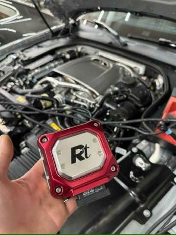 A person is holding a red device in front of a car engine.