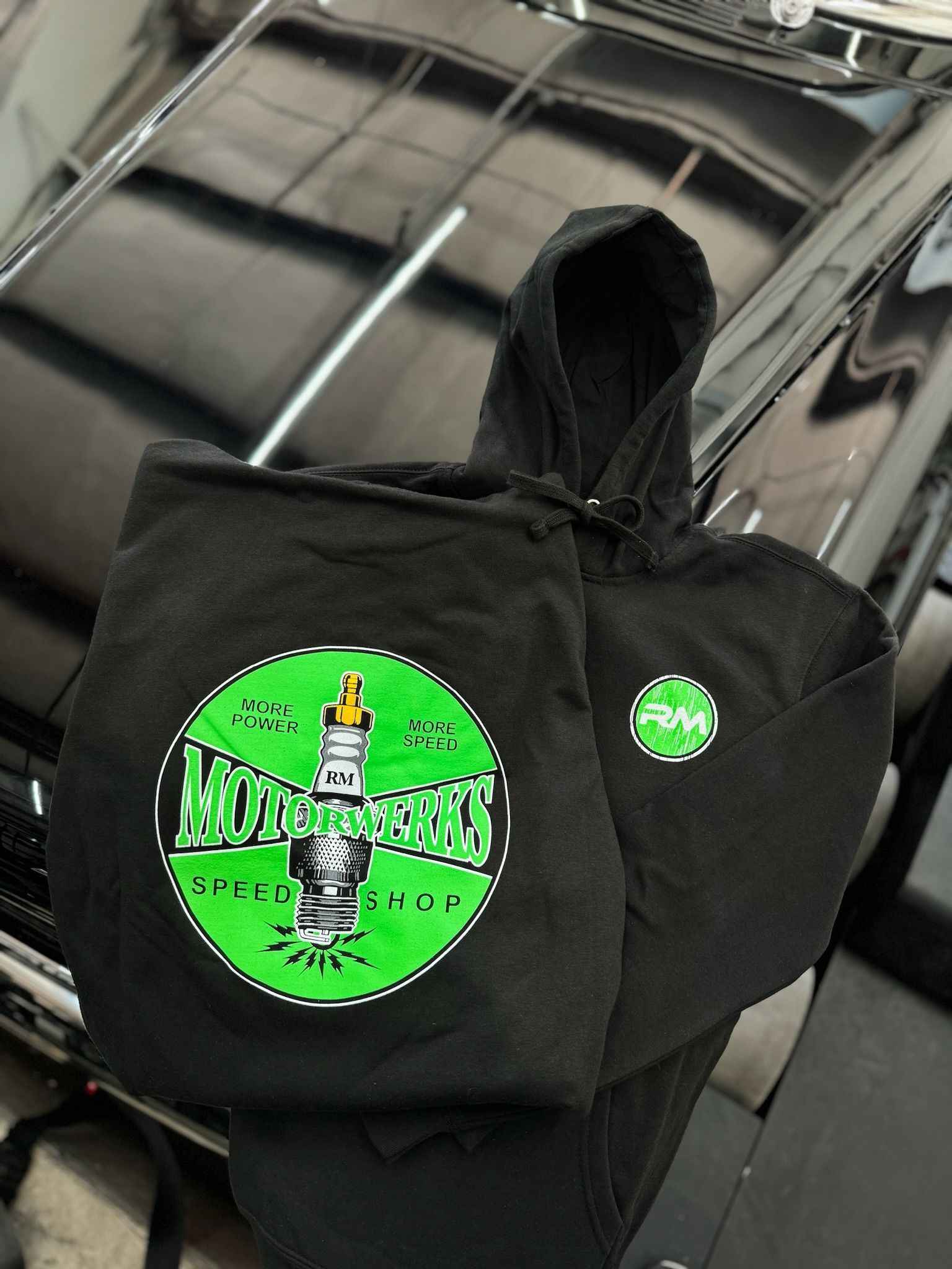 A black hoodie with a green logo is sitting in front of a black car.