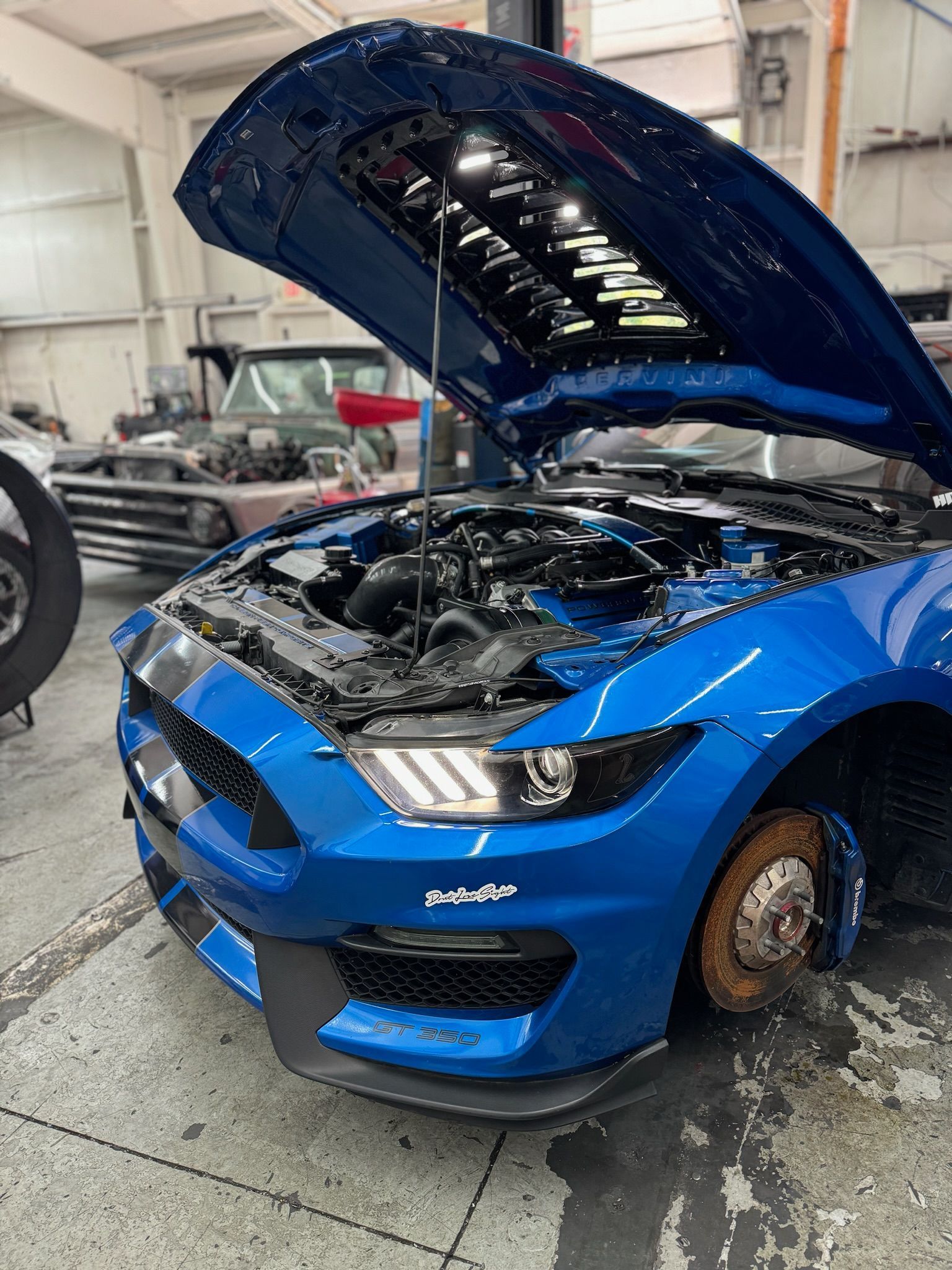 A blue ford mustang with the hood up in a garage.