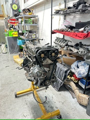 A motorcycle engine is sitting on a yellow stand in a garage.