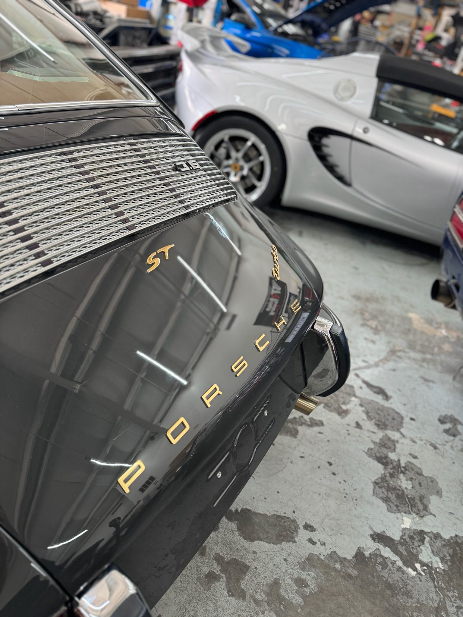 A black porsche is parked next to a silver car in a garage.