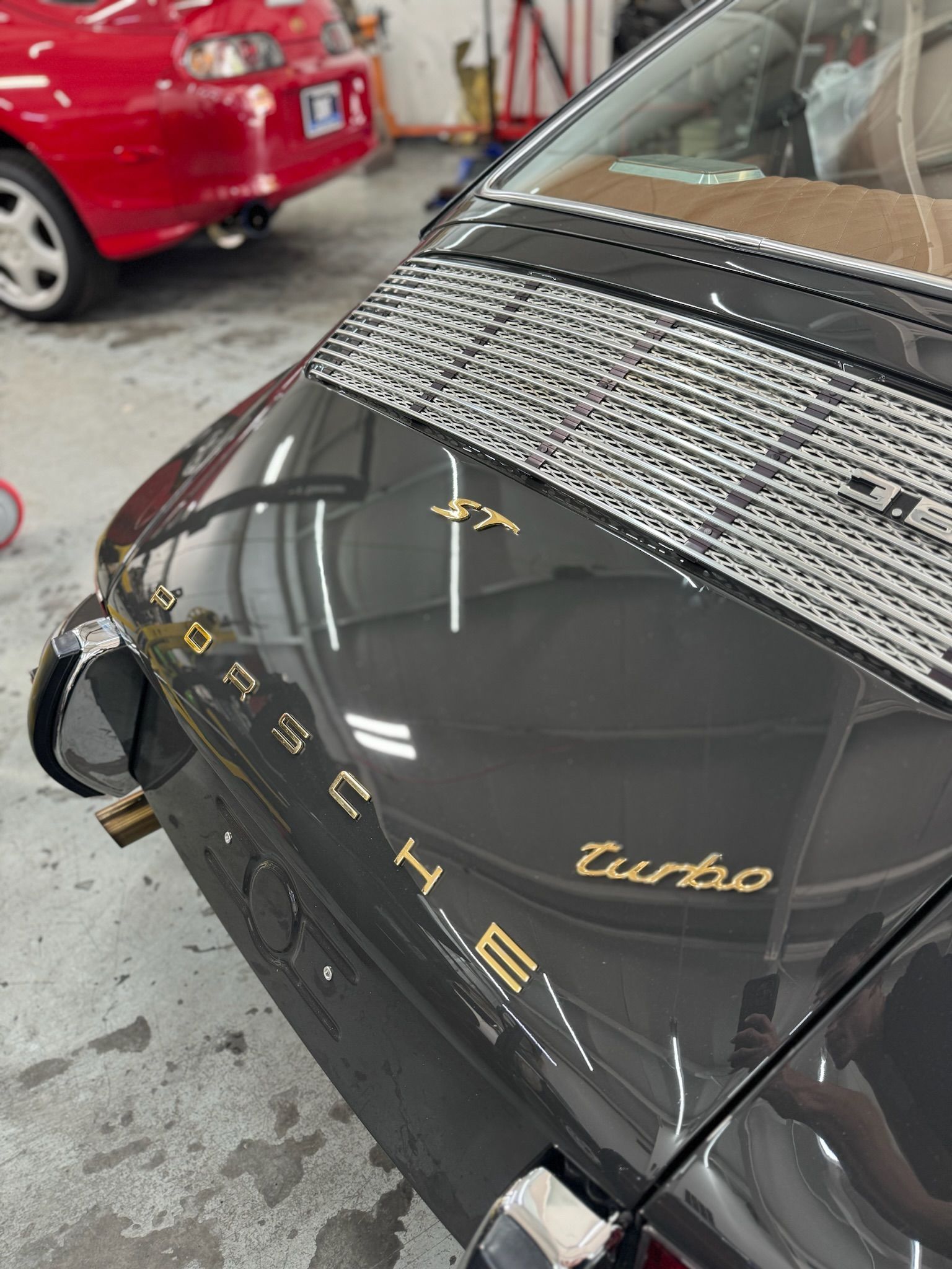 A black porsche turbo is parked in a garage next to a red car.