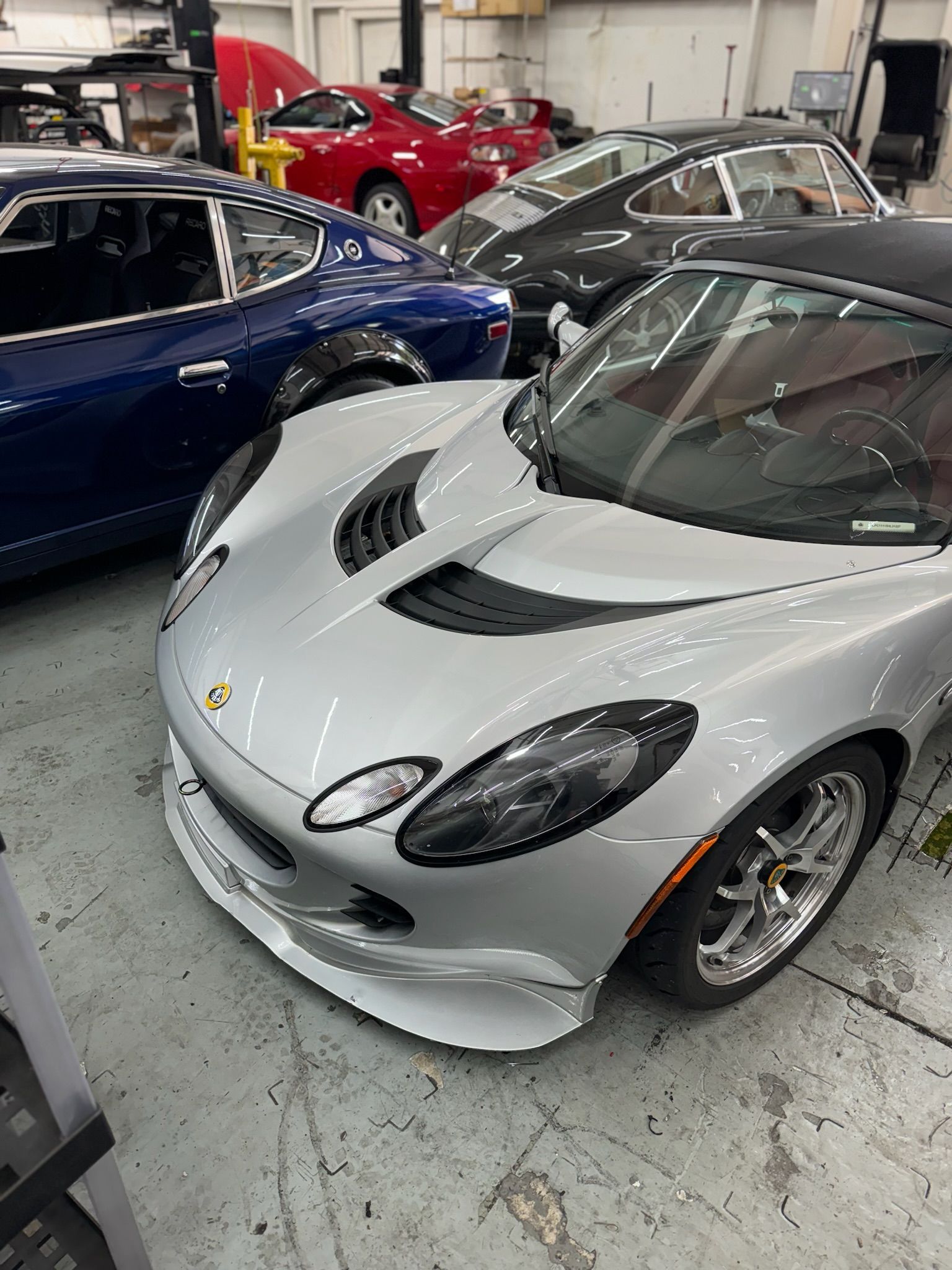 A silver sports car is parked in a garage next to other cars.