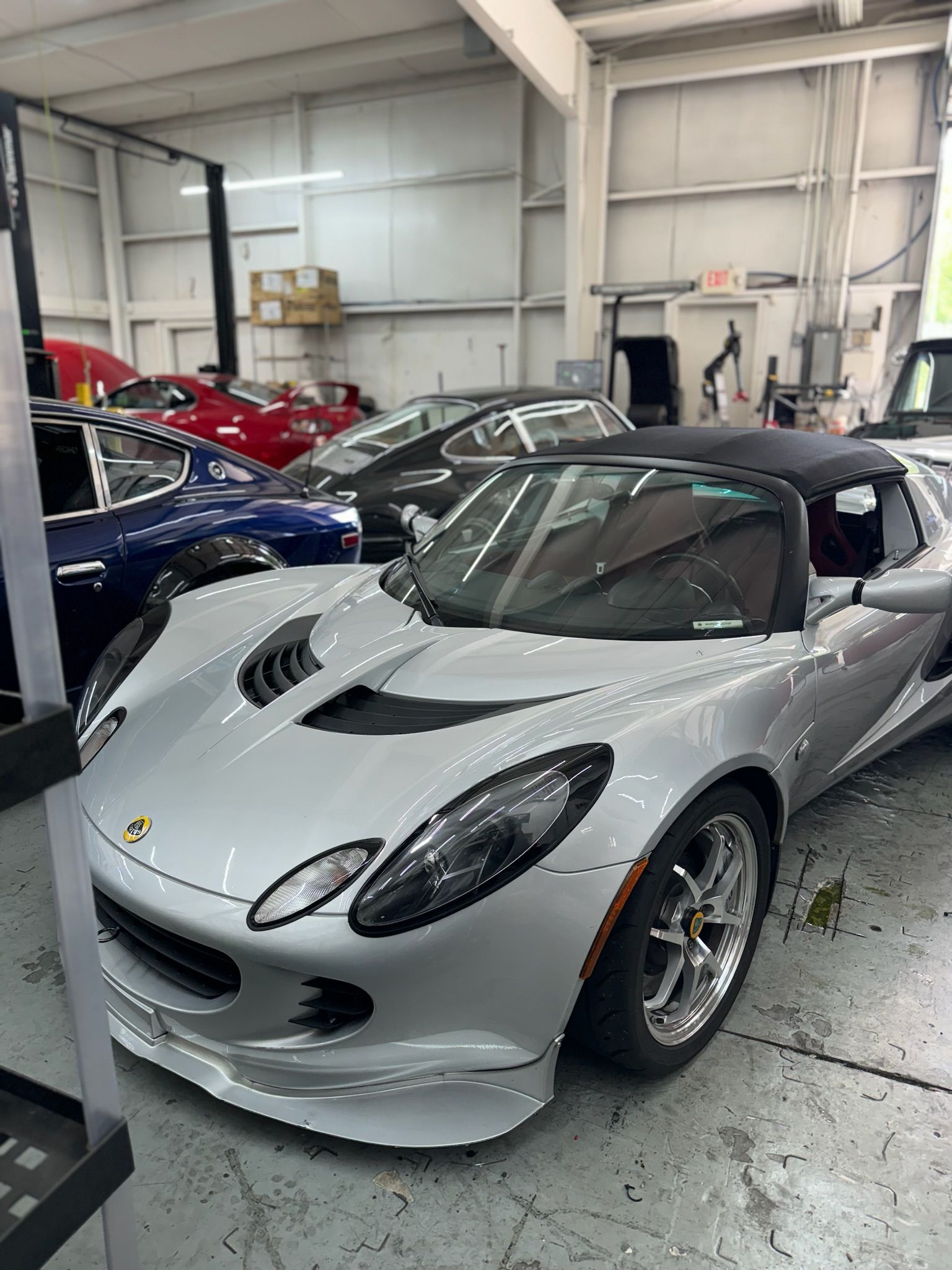 A silver sports car is parked in a garage next to other cars.