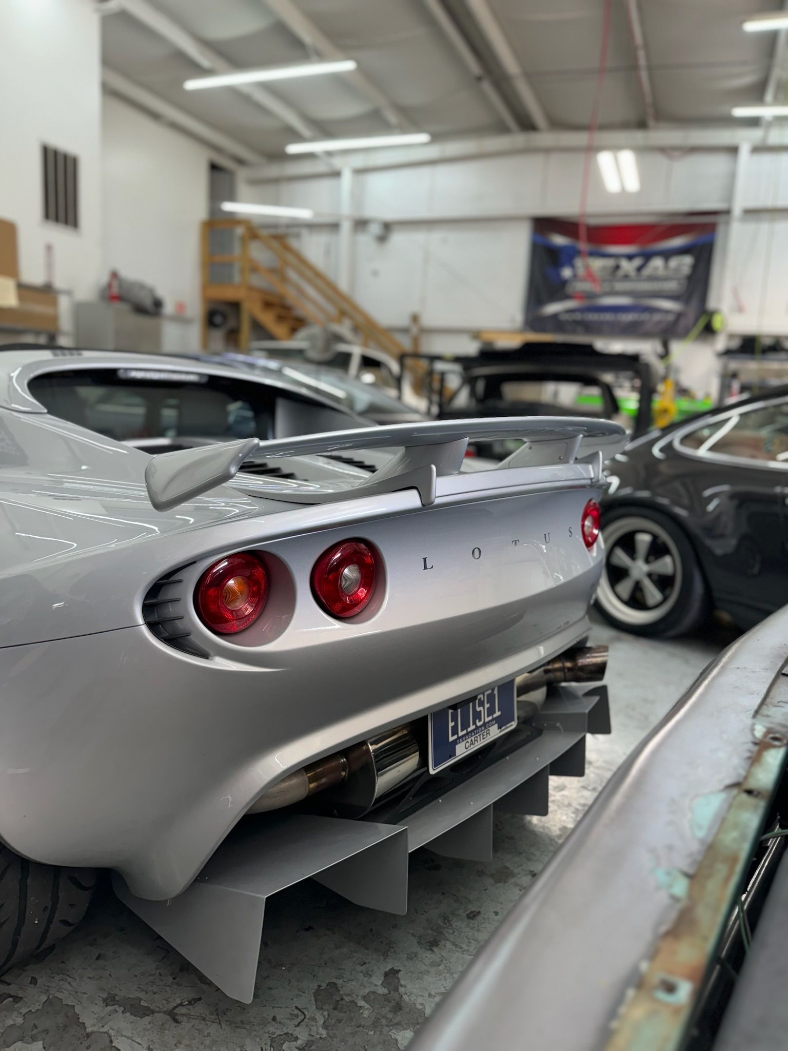A silver sports car is parked in a garage with other cars.