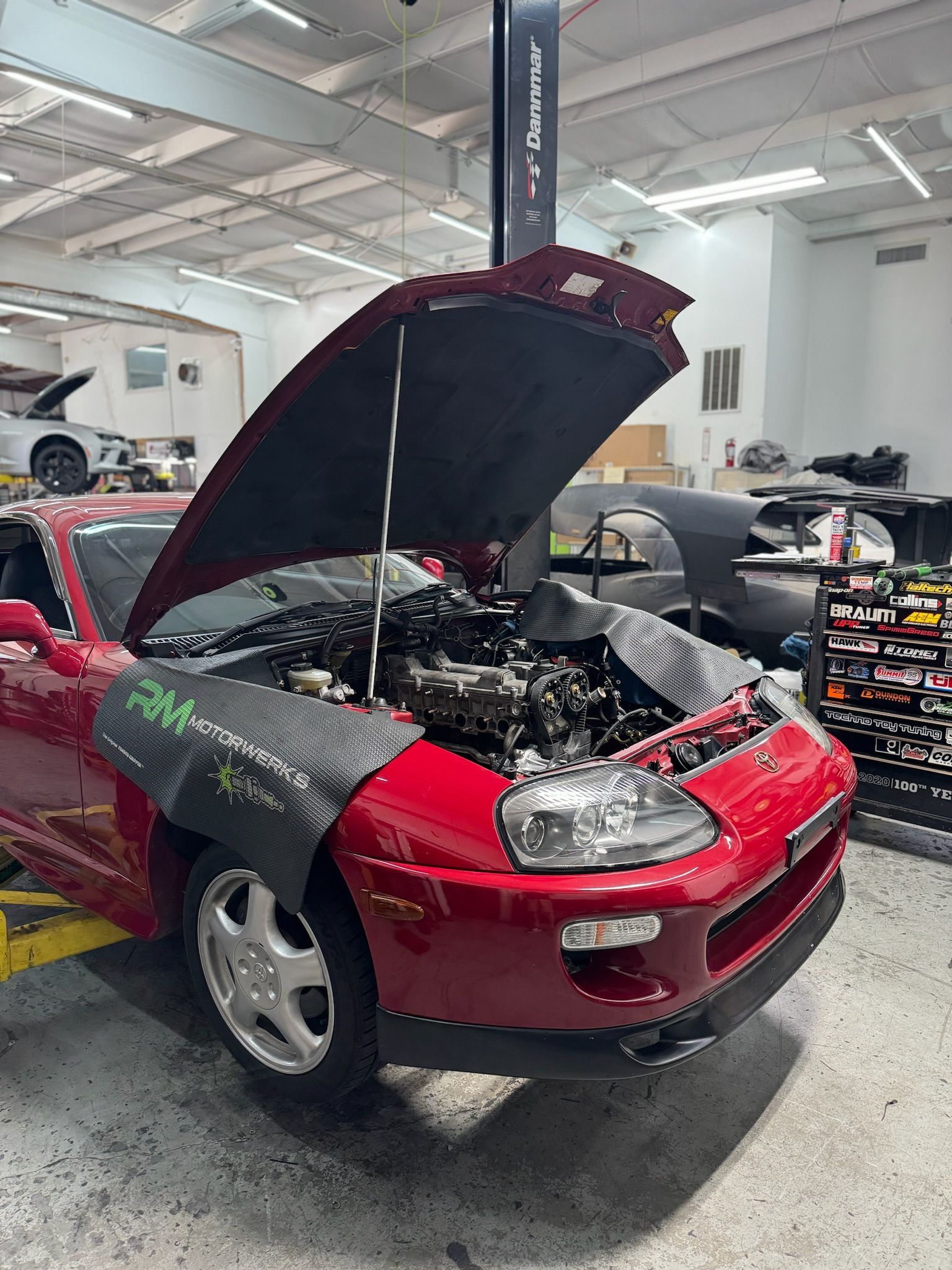 A red sports car with the hood up is being worked on in a garage.