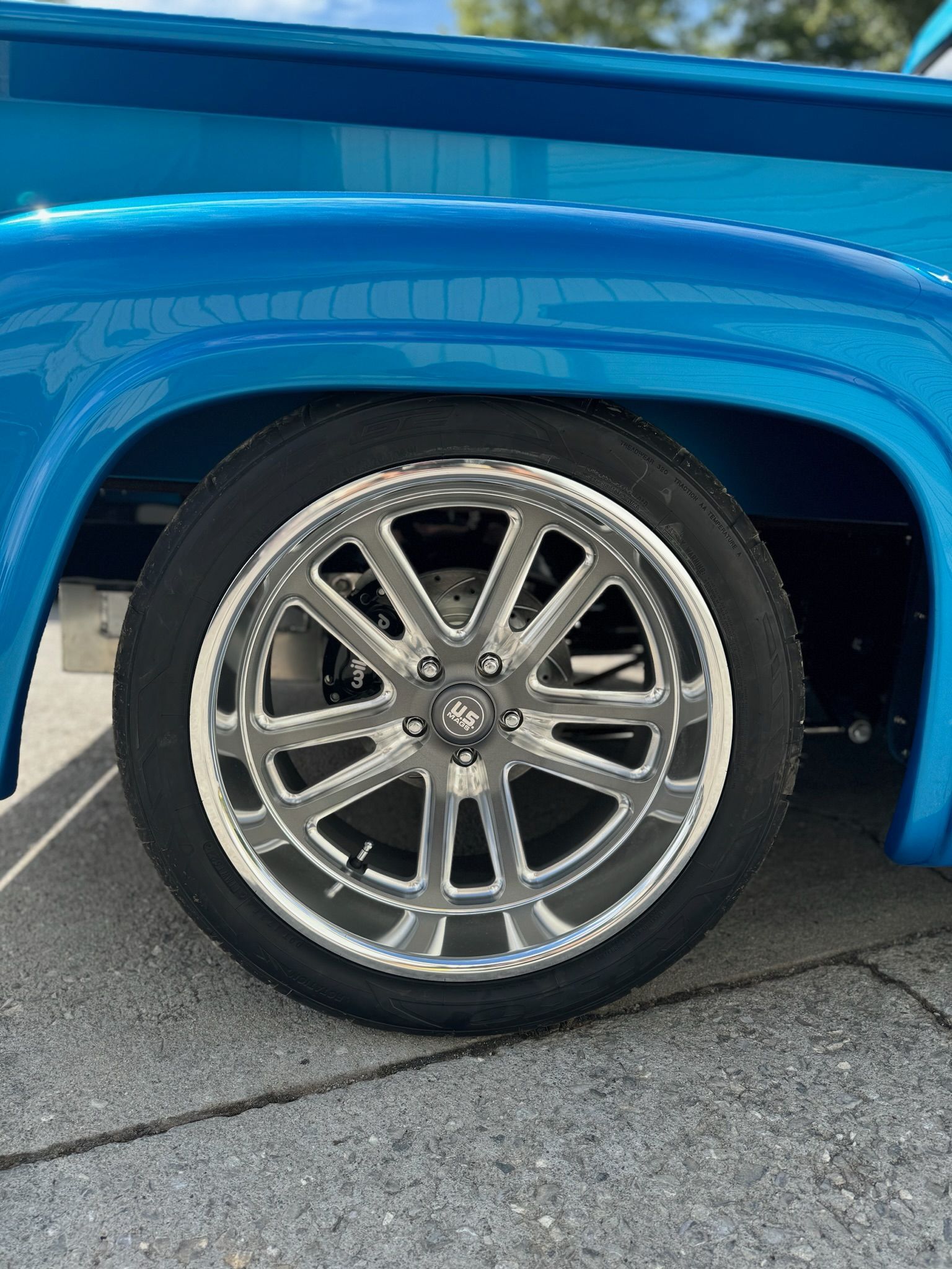 A blue truck with chrome wheels and tires is parked on the side of the road.