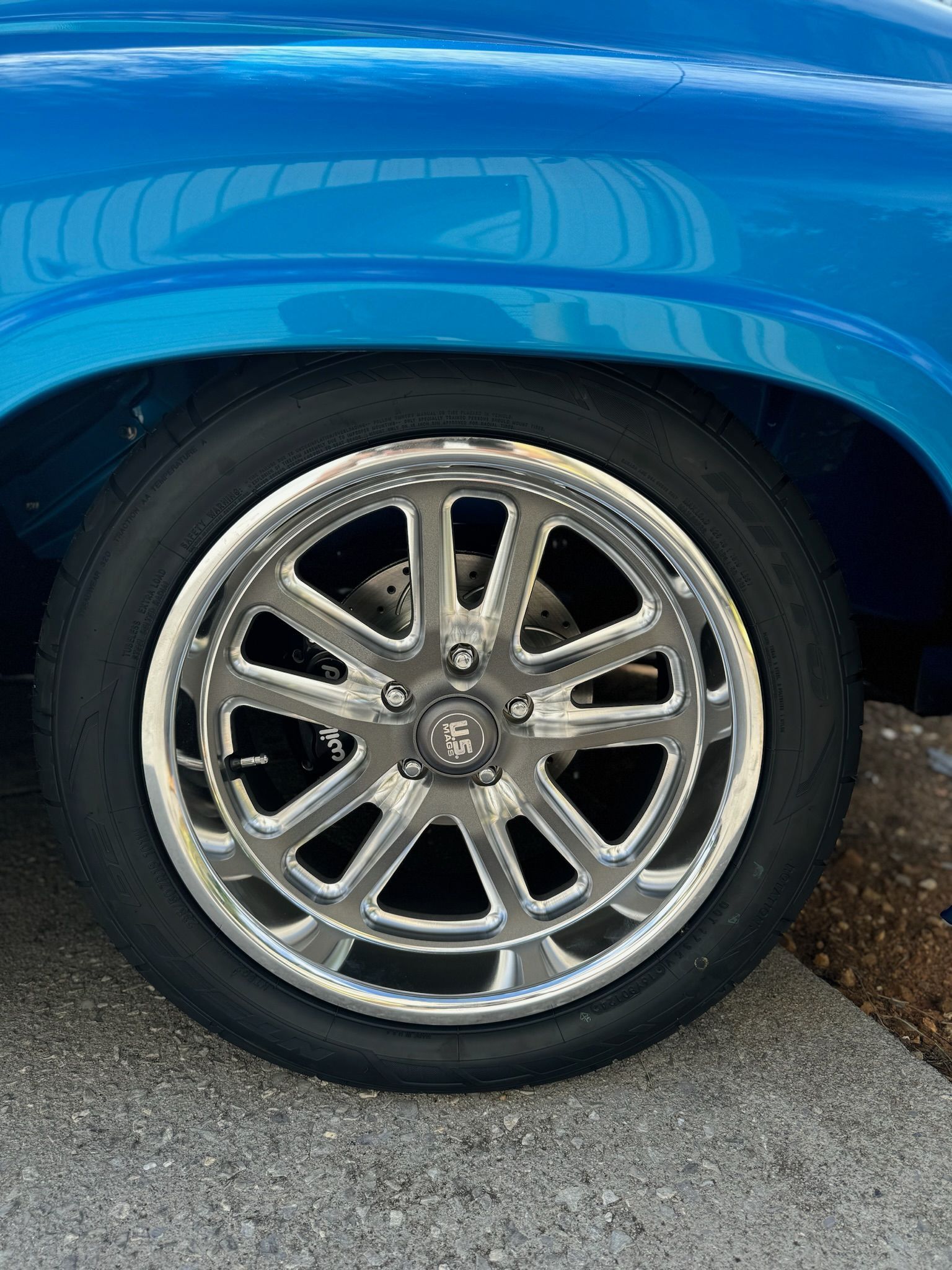 A blue truck with chrome wheels and tires is parked on the side of the road.