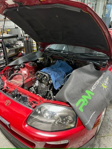 A red car with the hood open is being worked on in a garage.