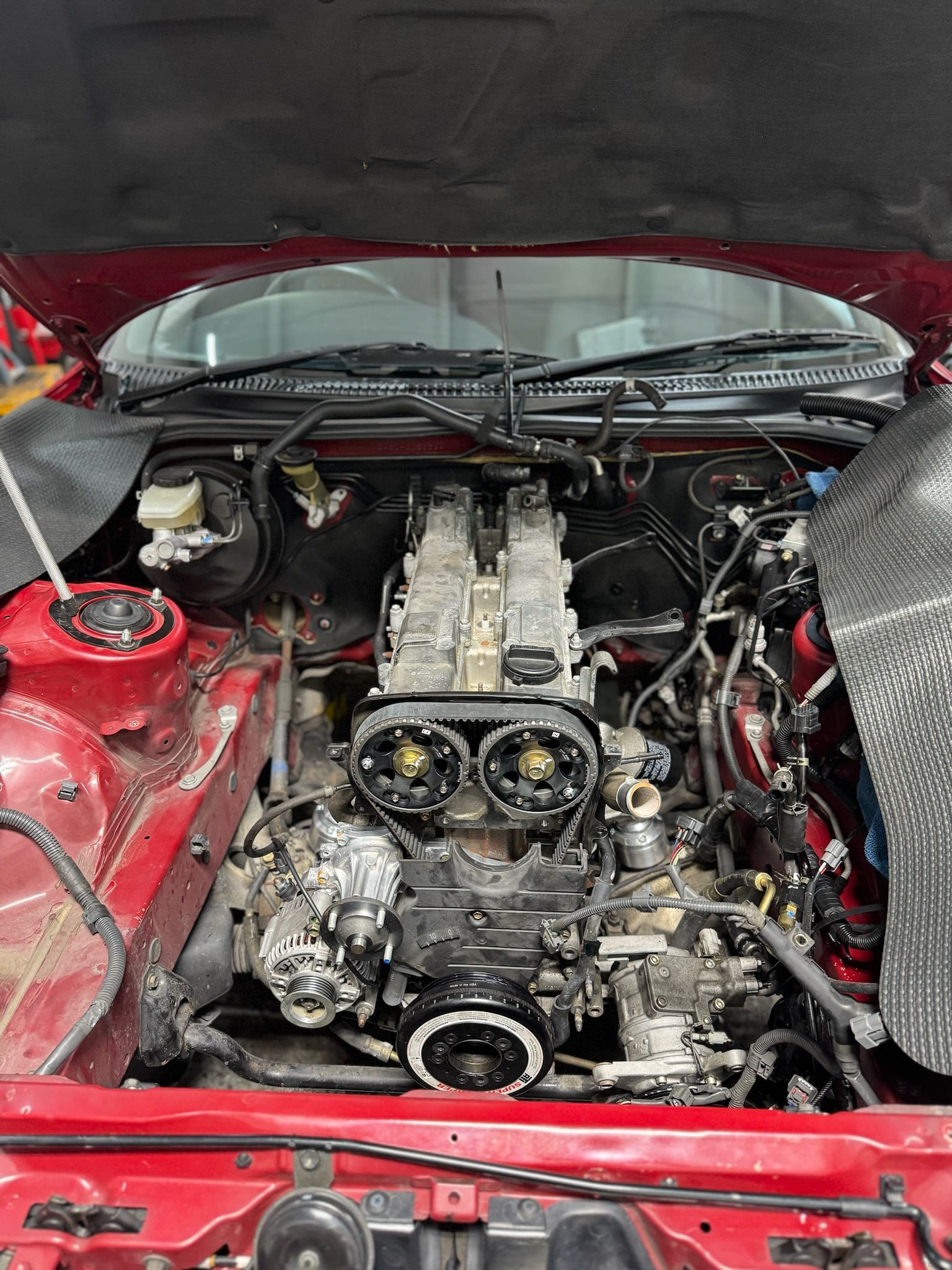 The engine of a red car is shown with the hood open.