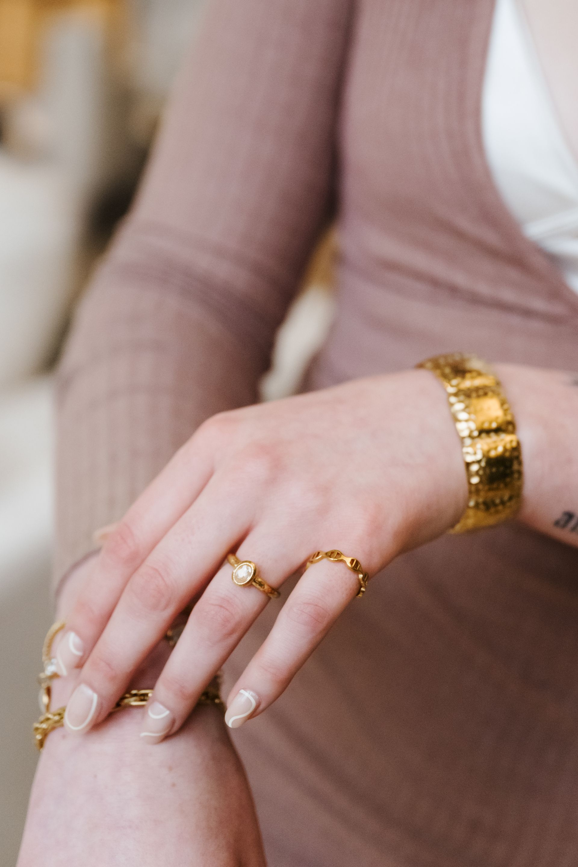 Close-up of a hand with gold rings and a bracelet resting on a pink ribbed sleeve.