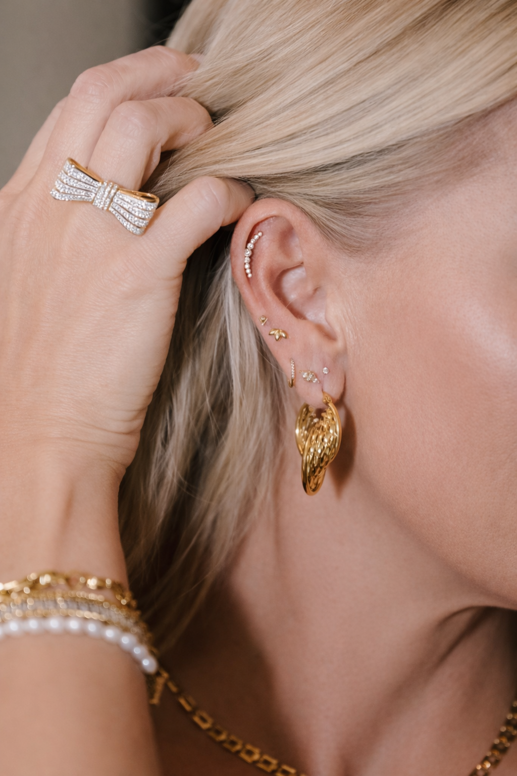 Close-up of a blonde woman wearing gold jewelry, adjusting her hair with a ringed hand.