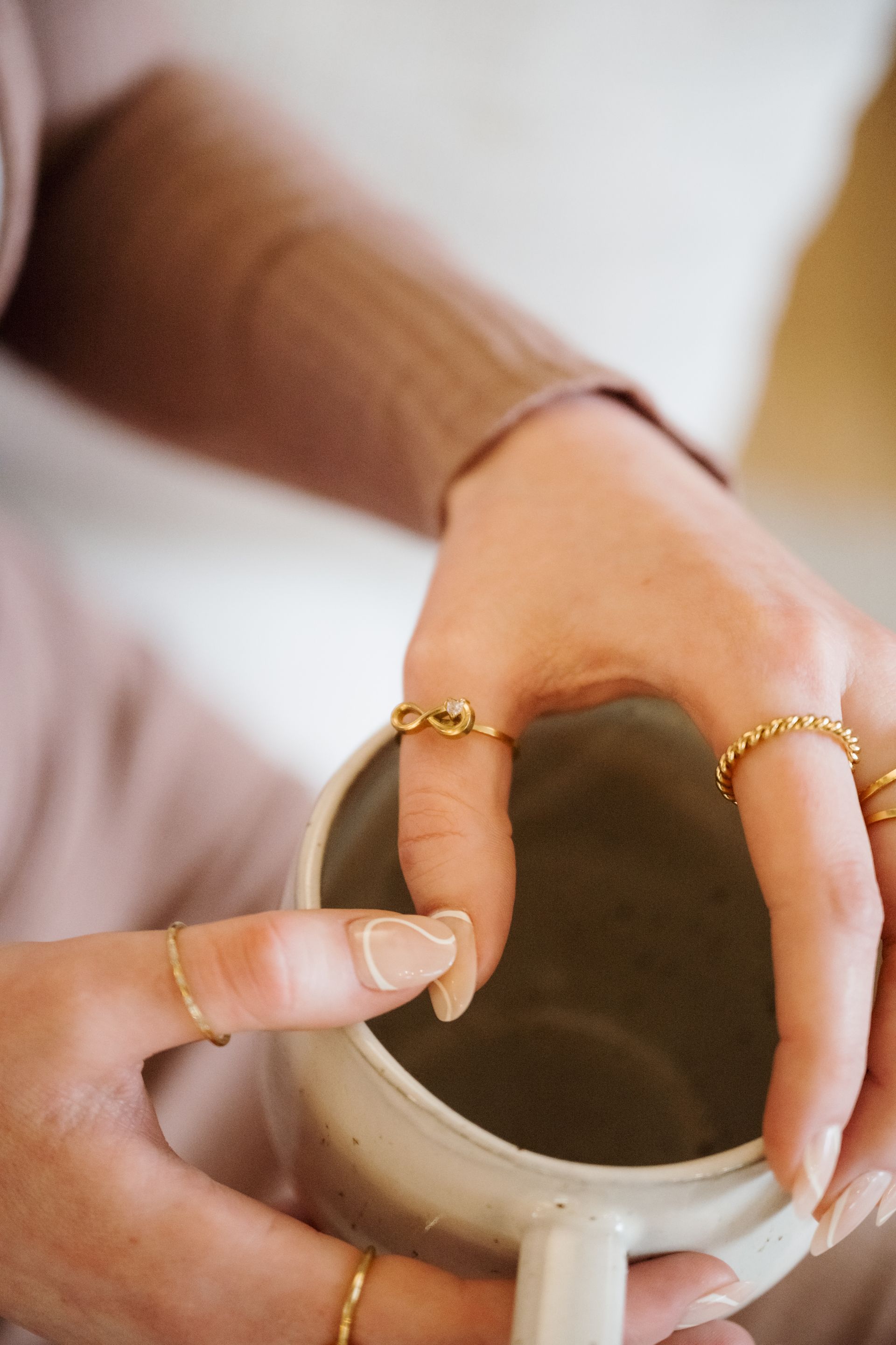 Hands with gold rings holding a white mug of dark coffee or tea