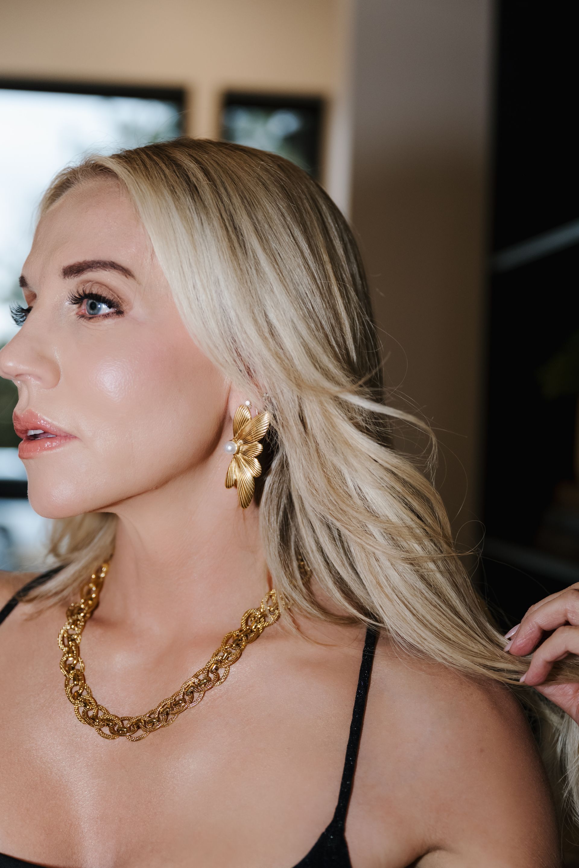 Blonde woman in a black top wearing gold jewelry, seen in profile indoors.