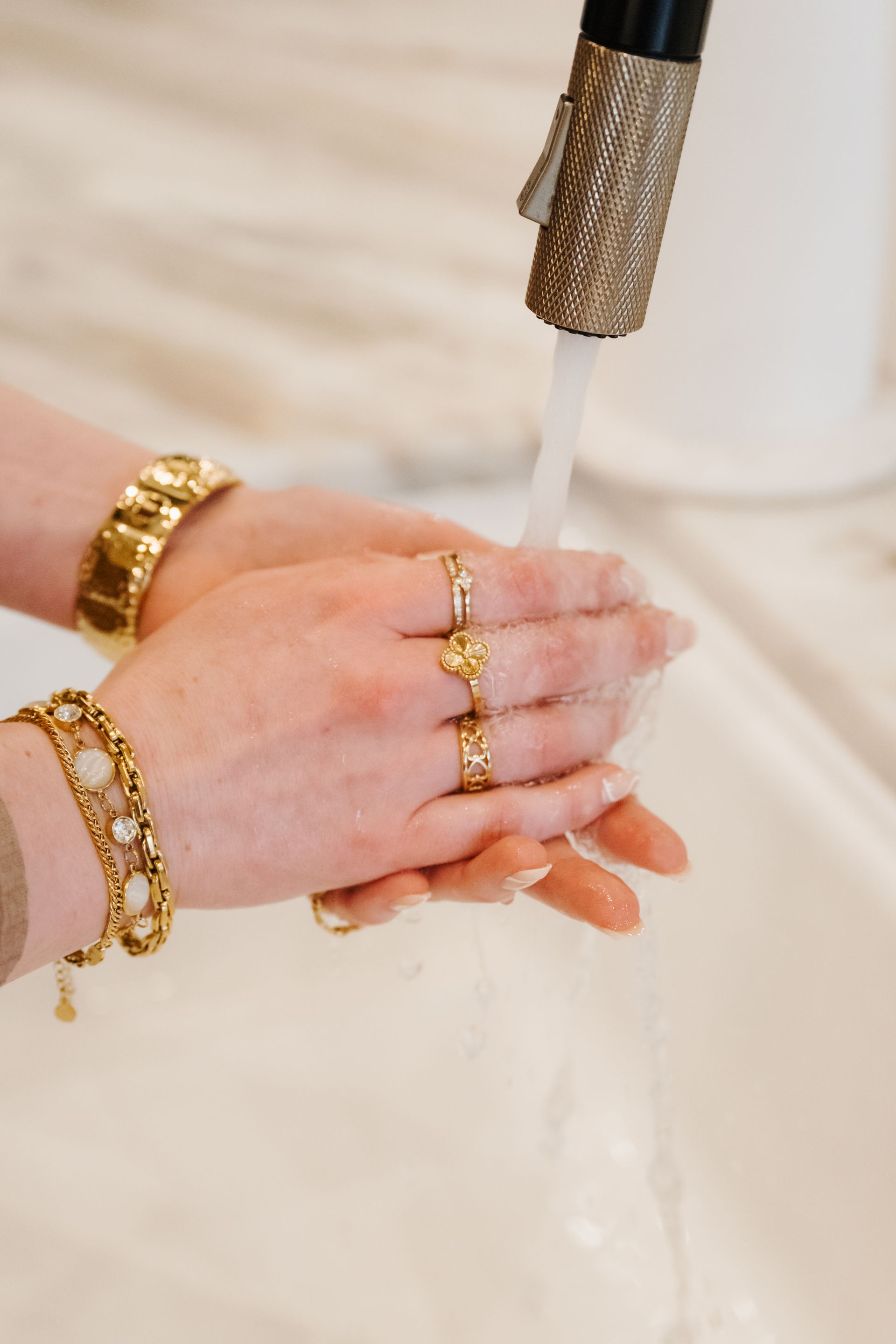 Hands with gold jewelry under running water at a sink