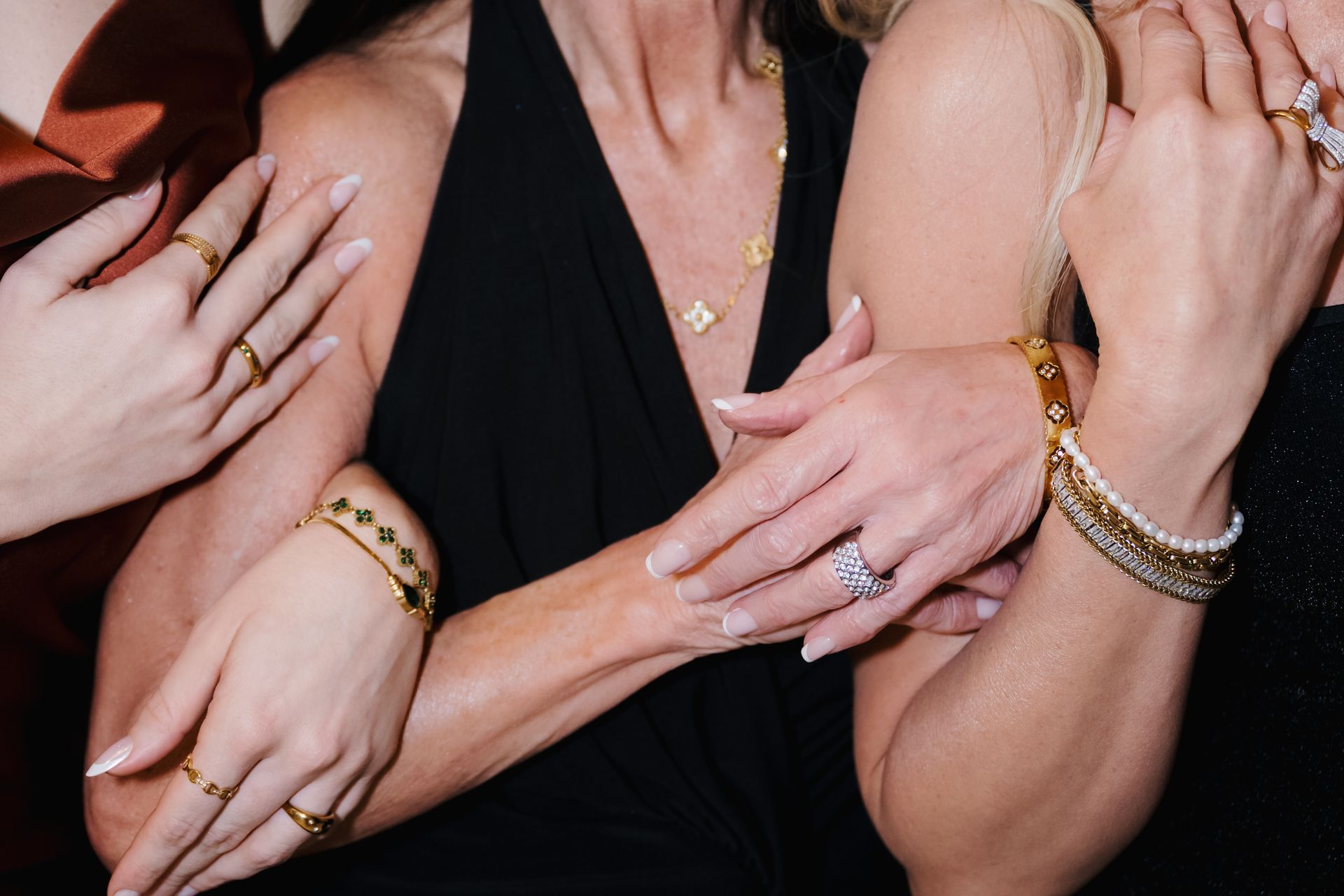 Close-up of four hands with rings and bracelets crossing over a black dress.