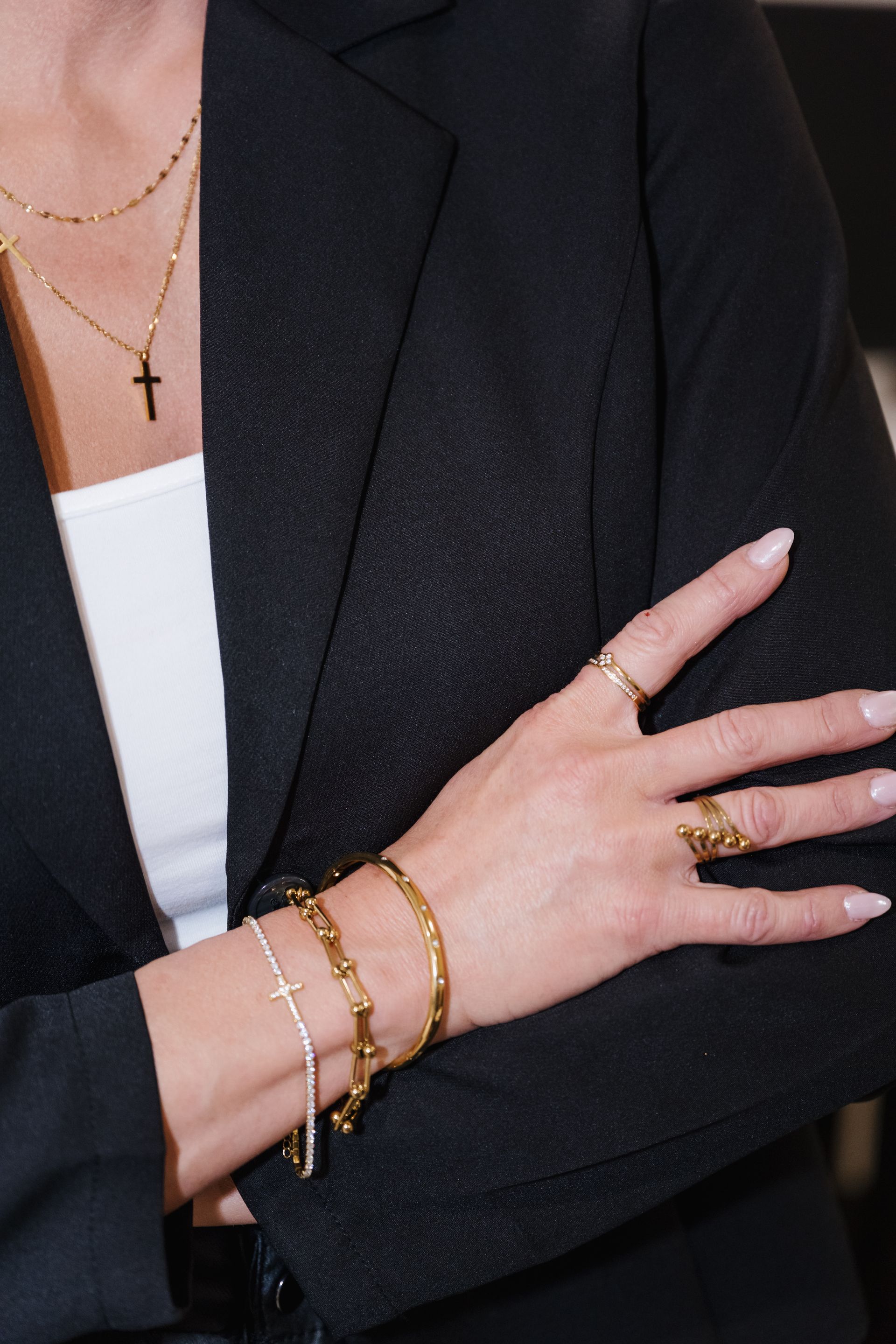 Close-up of a black blazer with a hand wearing gold bracelets and rings crossed over the arm