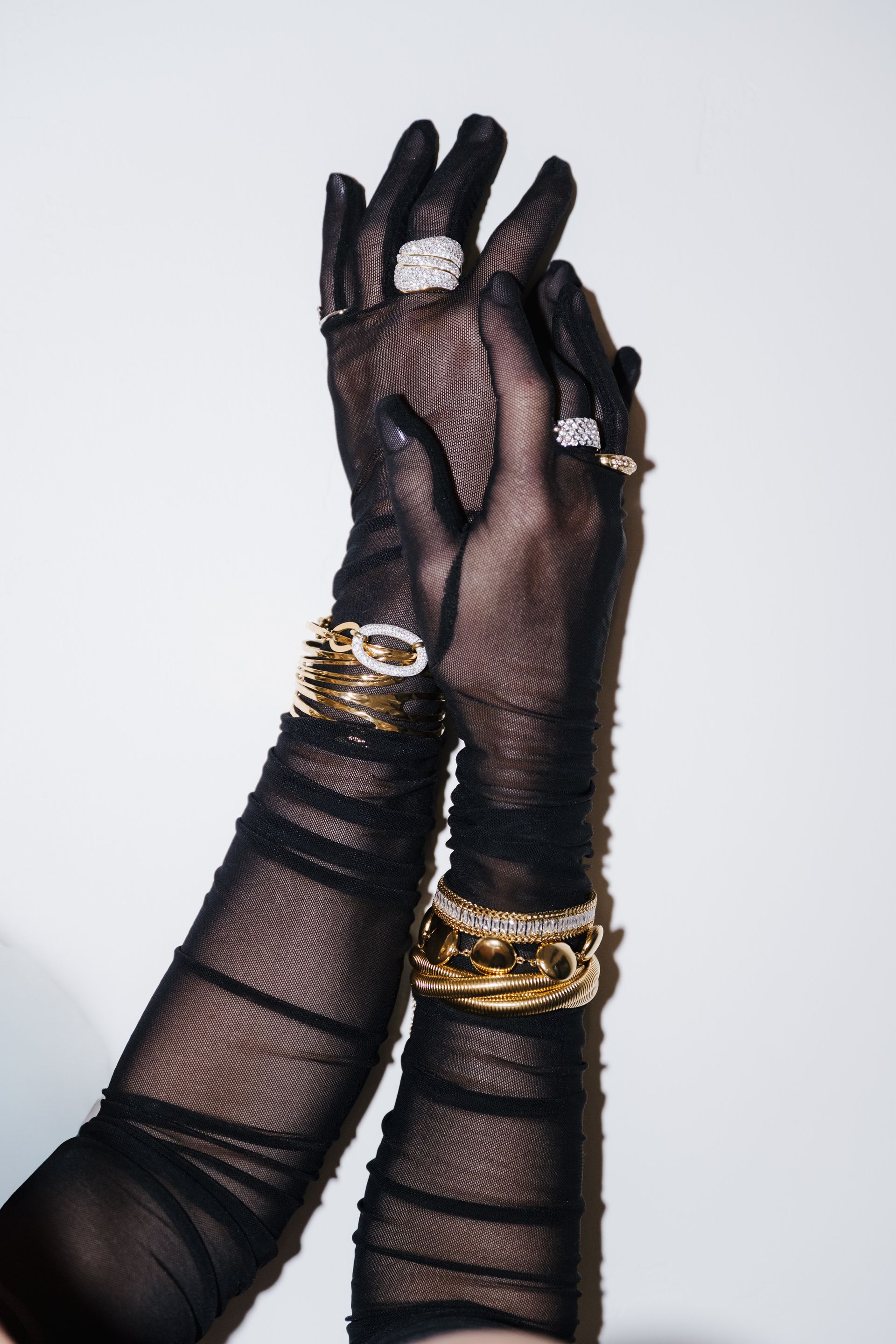 Black lace-gloved hands with gold bracelets raised against a light background