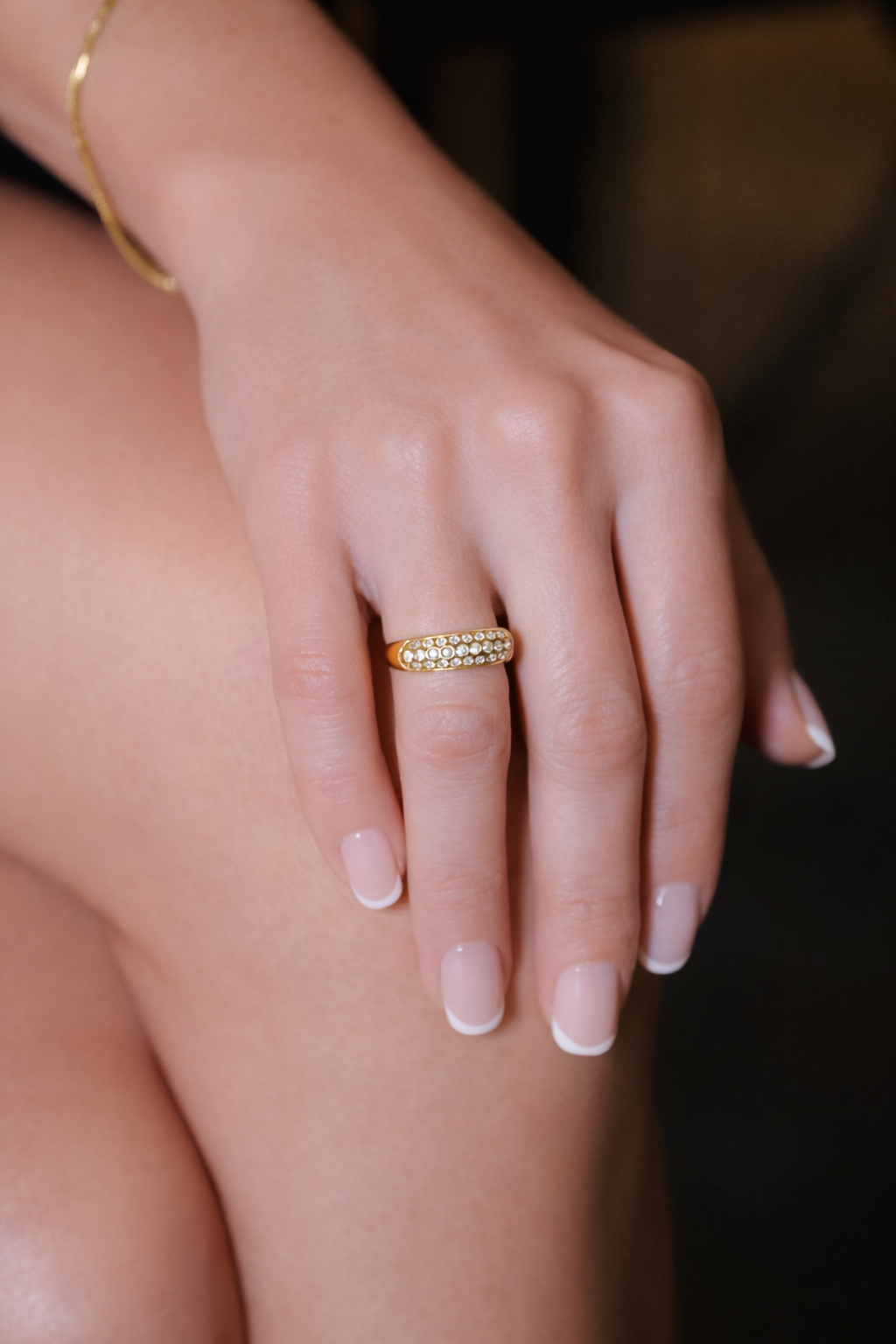 A hand with a gold ring resting on a bare thigh against a soft brown background
