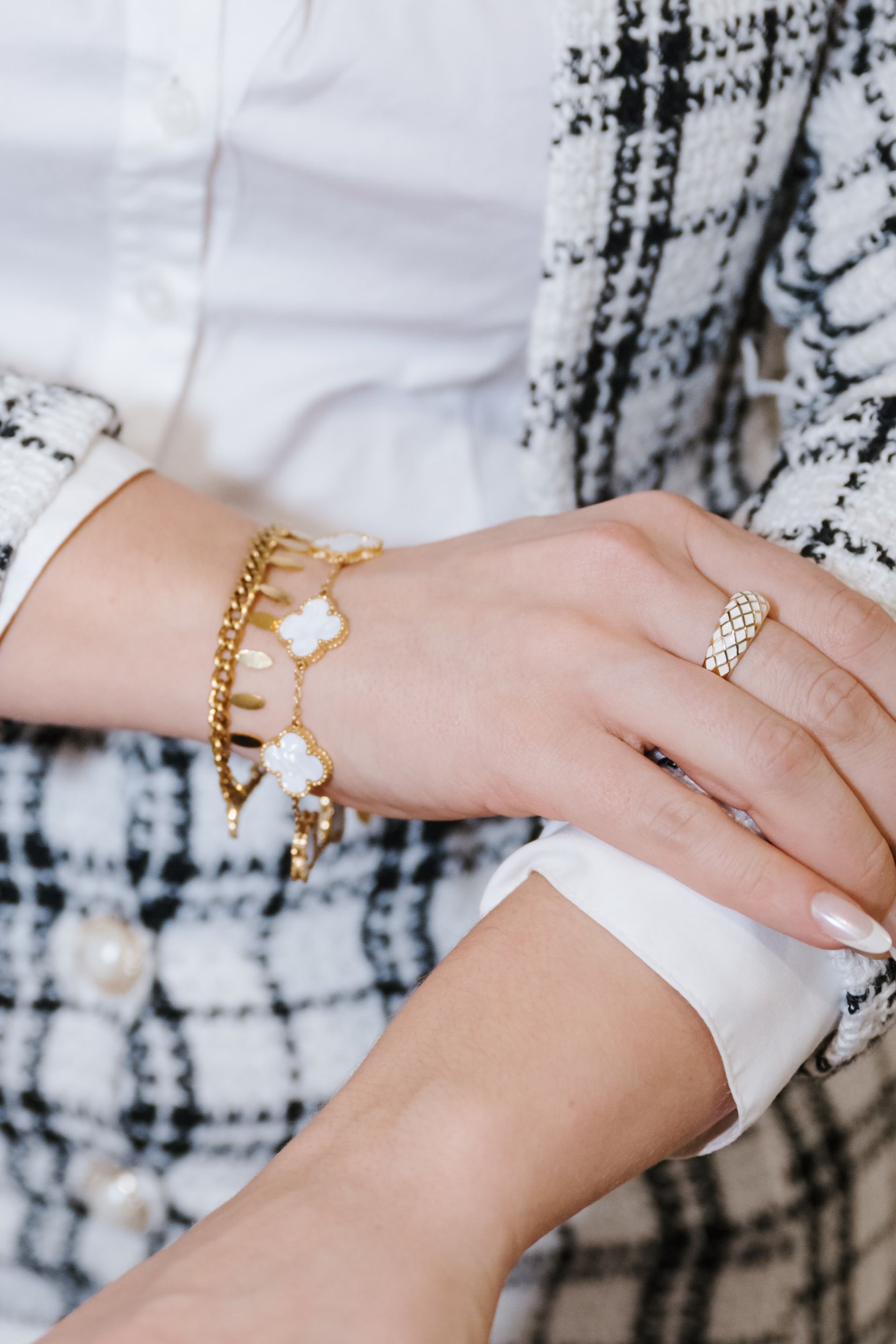 Close-up of crossed hands with gold bracelet and ring on a black-and-white plaid outfit