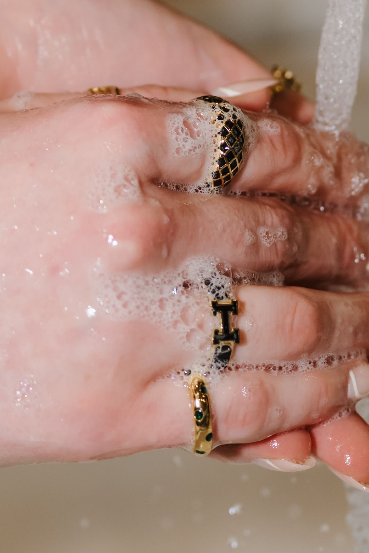 Handwashing close-up with soapy hands wearing gold rings under running water
