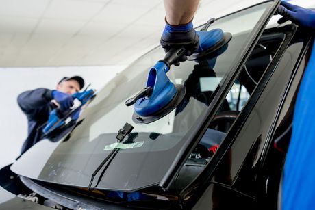 Two man is installing a windshield on a car.