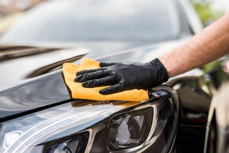 A person wearing black gloves is cleaning a car with a yellow cloth.