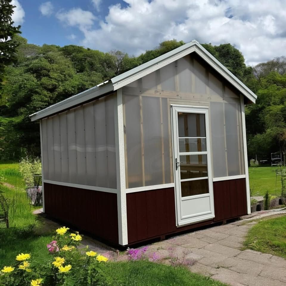 Brown and white shed with a white door, set on a stone path, surrounded by greenery.
