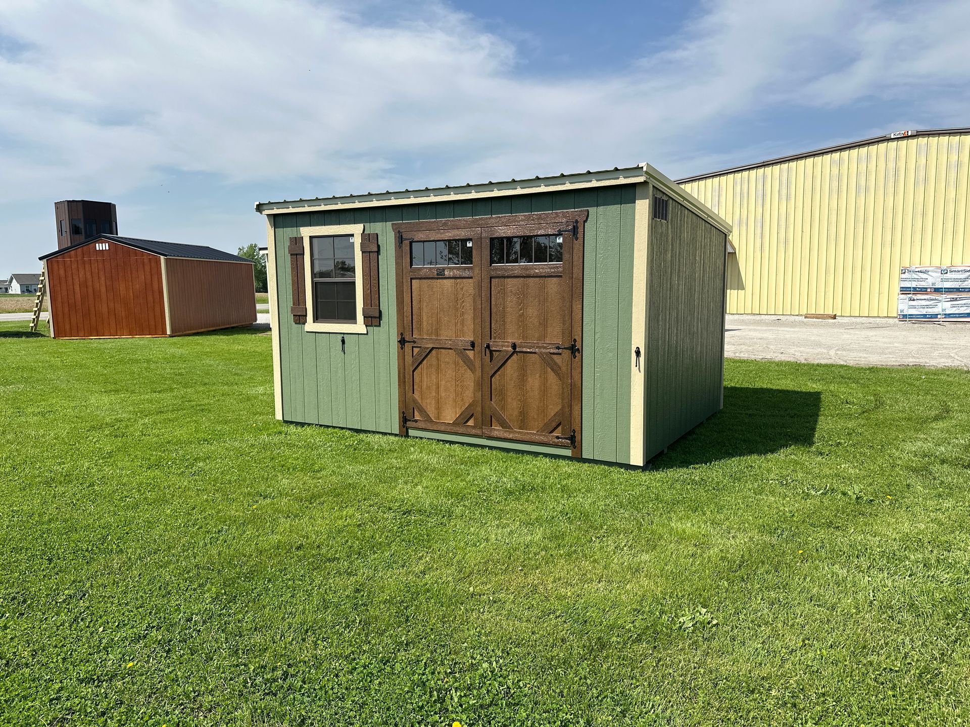 Green and brown shed on grass, with brown double doors and a small window.