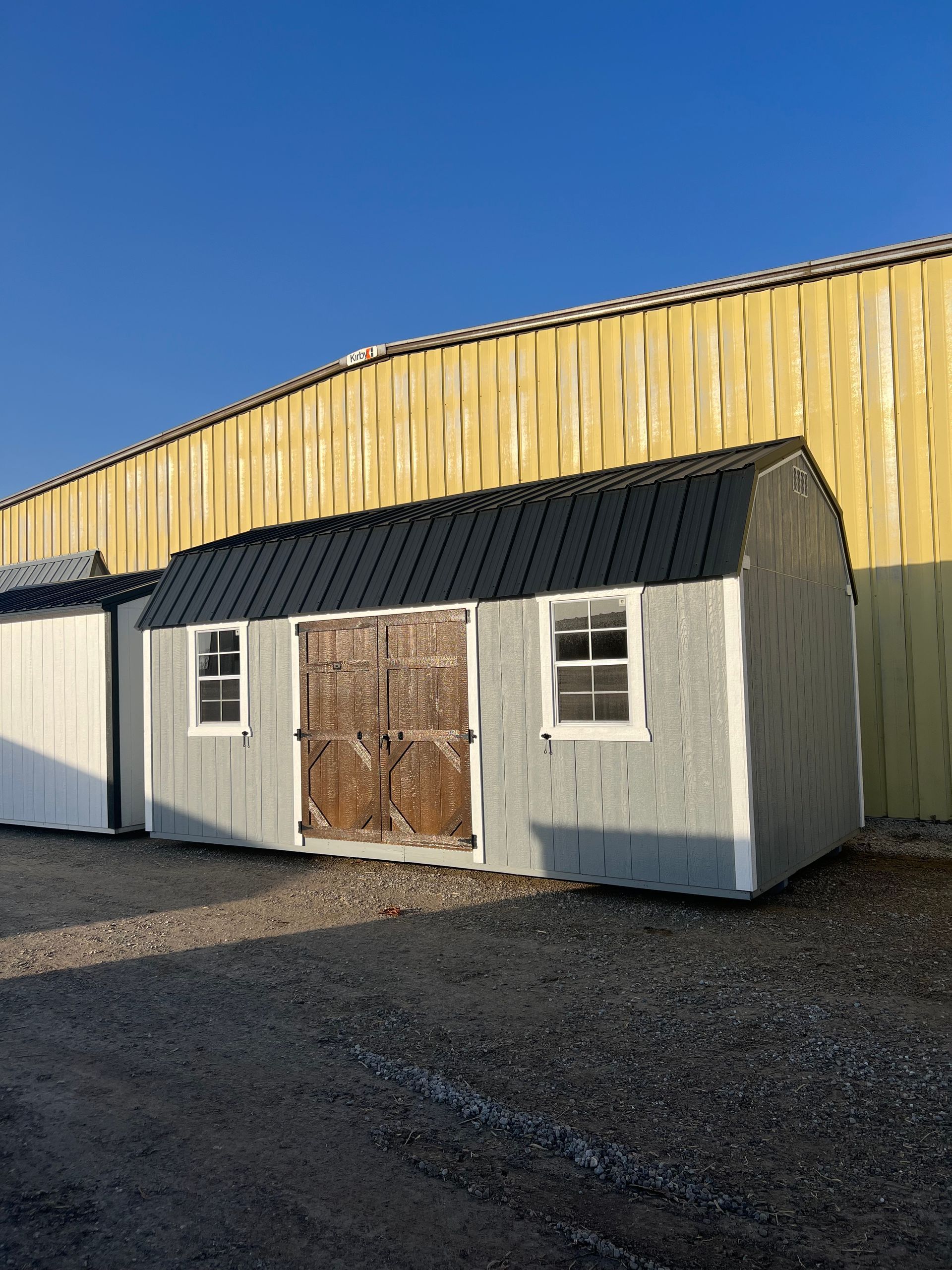 Grey shed with arched roof, two windows, and brown double doors, set against a yellow wall.