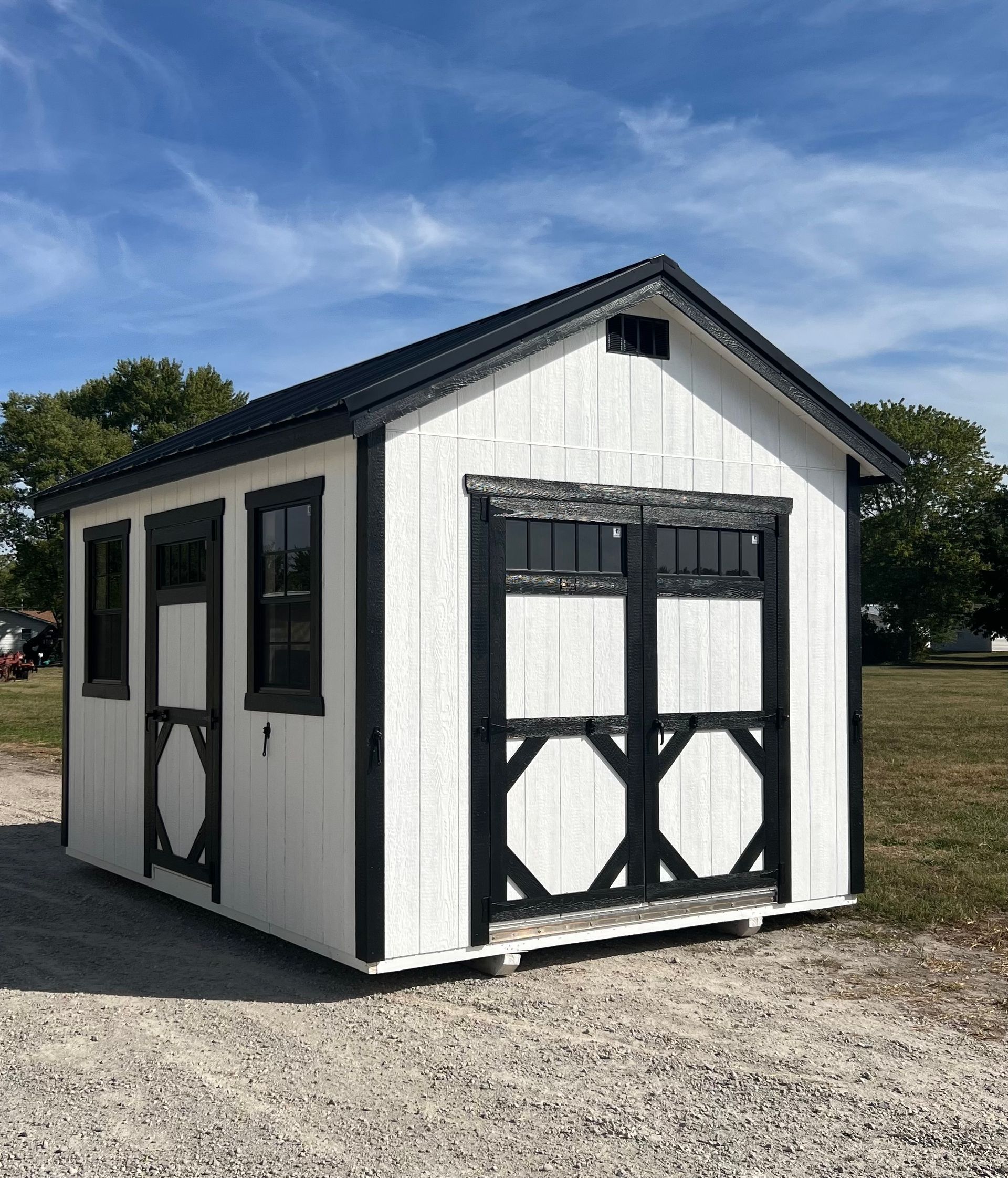 White shed with black trim and door, set on gravel, under a blue sky.